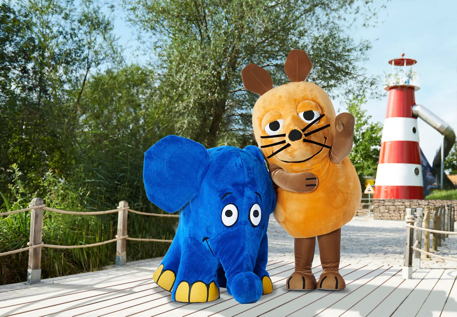 Maus und Elefant im Ravensburger Spieleland vor dem rot-weißen Leuchtturm